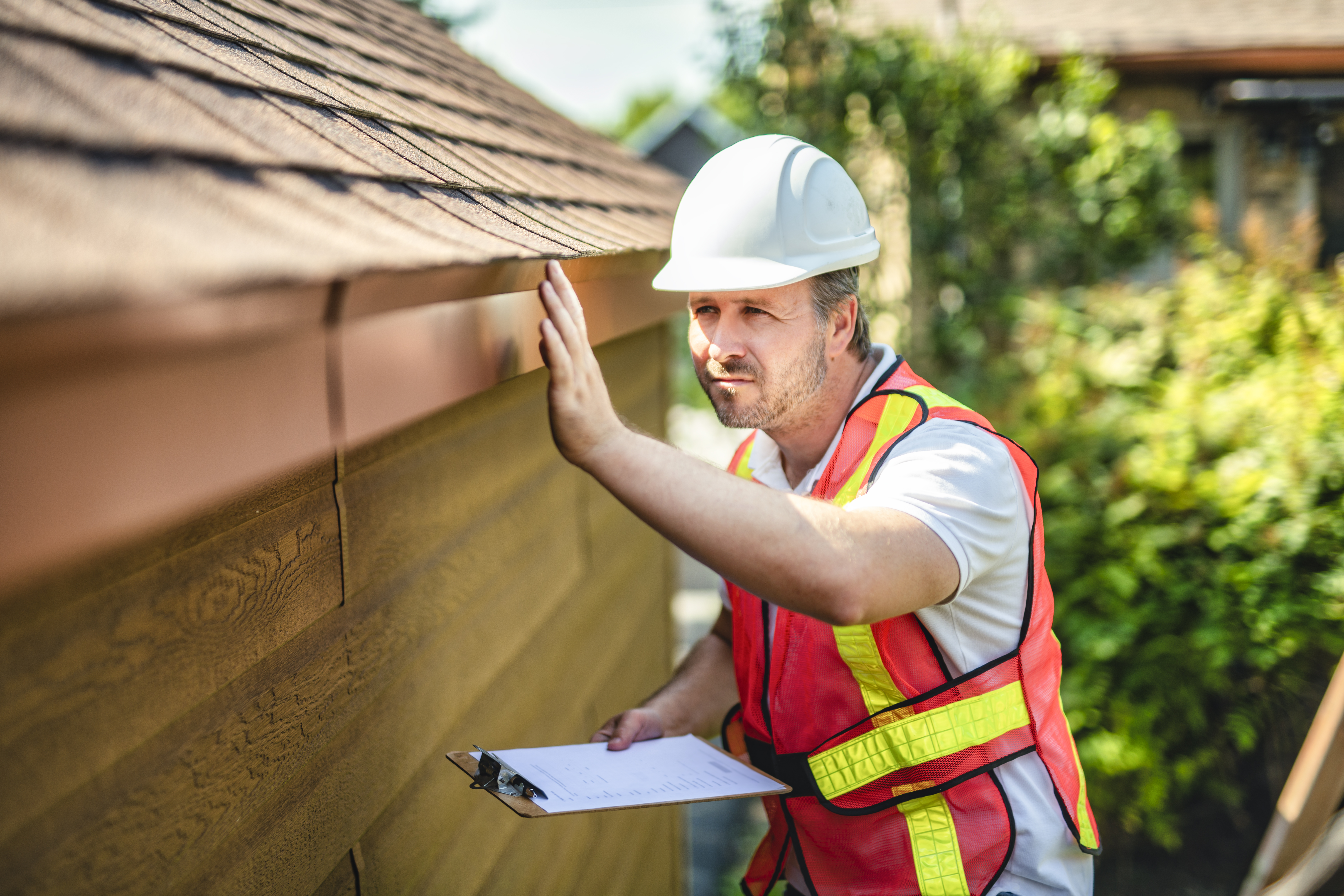 A person wearing a safety vest and a hard hat inspecting the roof of a home